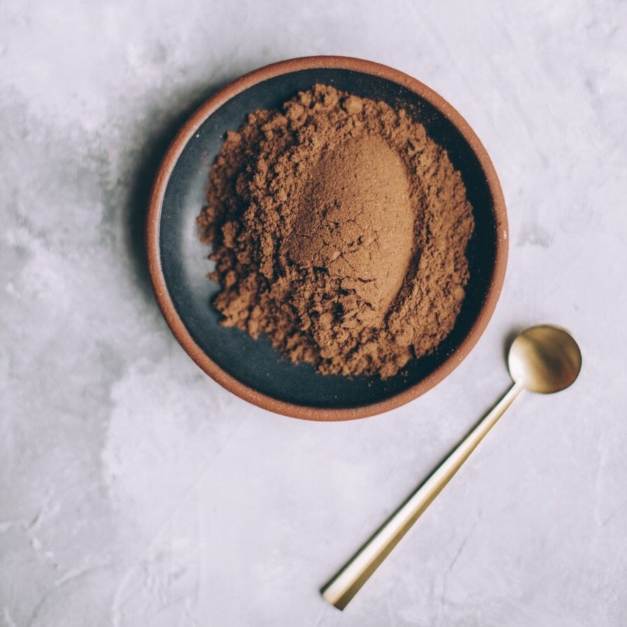 Bird's eye view of brown Pau D'Arco powder on a dark plate next to a golden spoon on marbled table. North Glow