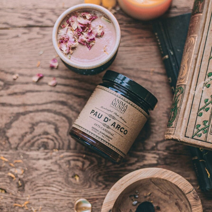 Anima Mundi screw top jar Pau D'Arco lies on a wooden table next to a cup and books, bird's eye view.