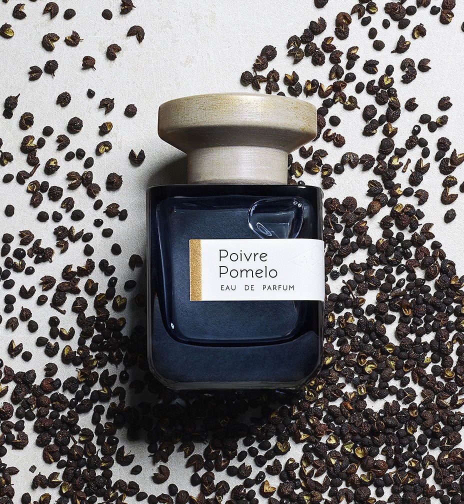 Dark blue glass bottle with gray lid "Poivre Pomelo" by Atelier Materi surrounded by peppercorns.