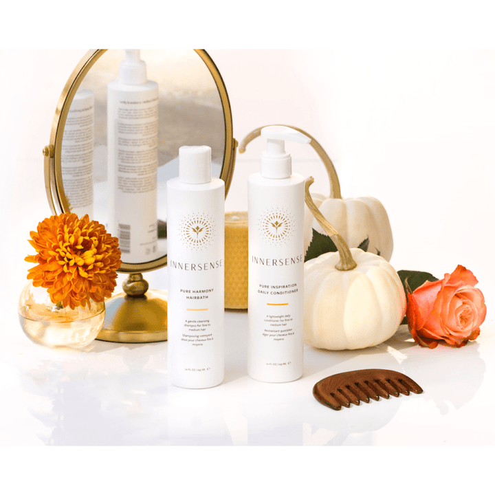 Innersense Pure Harmony Shampoo and Contitioner Bottles Standing in front of a mirror with comb and flower decoration.