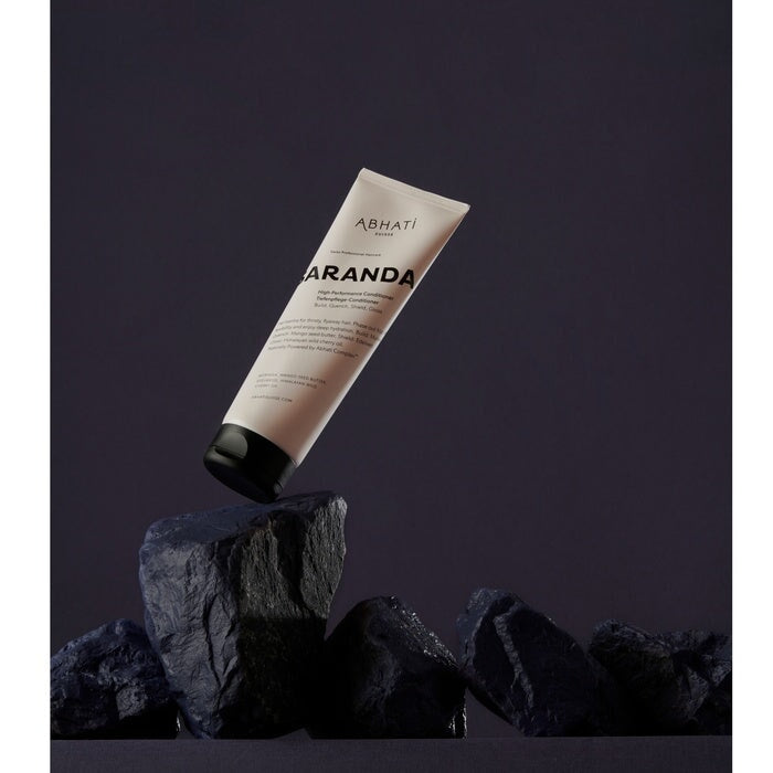 Abhati Suisse Saranda Conditioner Tube steht auf schwarzen Steinen. North Glow