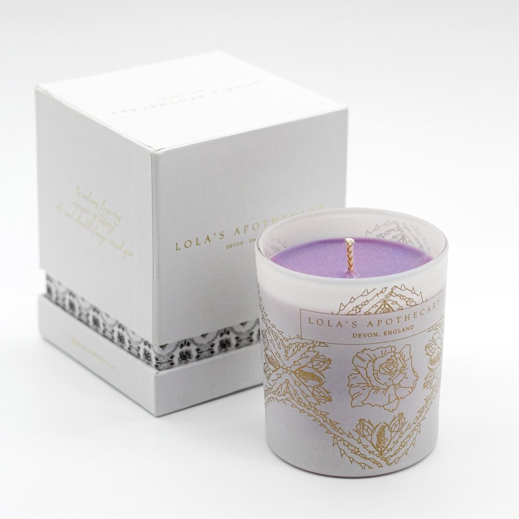 Lola's Apothecary Sweet Lullaby Duftkerze im verziertem Milchglas steht neben der Verpackung vor weißem Hintergrund. North Glow