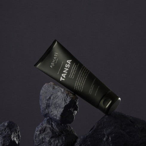 Abhati Suisse Tansa Shampoo Tube lehnt schräg an dunklen Steinen.