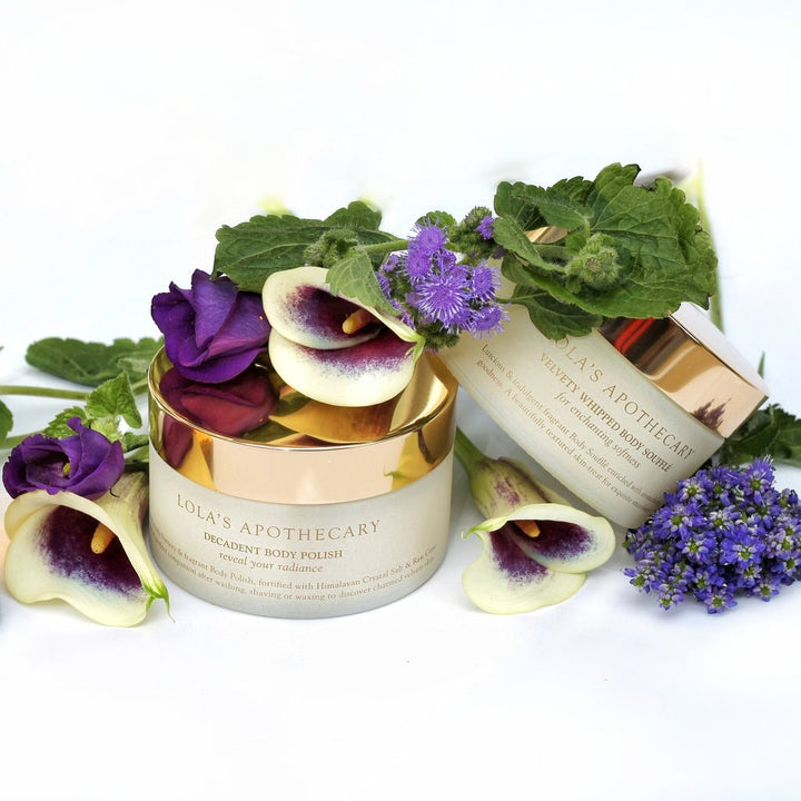 2 Glastiege Lola's Body Soufflé und Body Polish stehen geschmückkt mit Blumen auf weißem Untergrund.