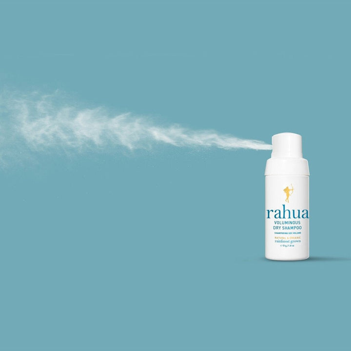 Rahua Voluminous Dry Shampoo against a blue background sprays dry shampoo.